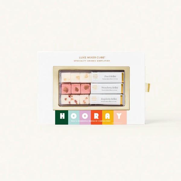 A boxed set of Luxe Mixer Cubes for specialty drinks, featuring three flavors: Peach Bellini, Strawberry Bellini, and Raspberry Bellini. The box includes colorful text that says "HOORAY" and highlights making mimosas in simple steps.