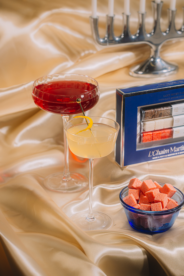 Two cocktails on a table with a box of L'Chaim Martinis and a bowl of watermelon cubes.