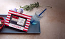 A Luxe Mixer Cube set with red, white, and blue packaging, featuring three mixer cubes labeled Tart Cherry, Shimmering White Raspberry, and Blueberry, accompanied by a glass of blue drink with ice and straw, and a small bowl of colorful sugar cubes.