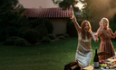 Two women celebrating outdoors with drinks in a garden setting.