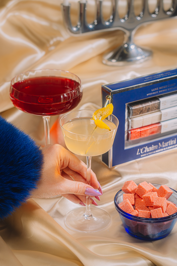 Two cocktails on a table with a box of matches and a bowl of pink cubes.