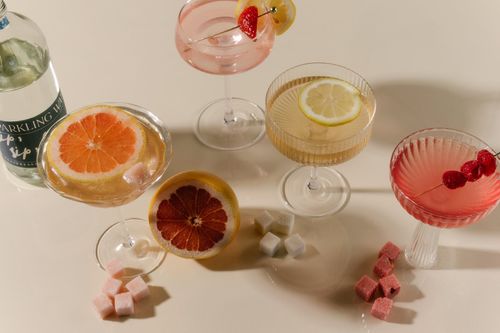 A variety of colorful cocktails in glassware, accompanied by citrus slices and Luxe Mixer Cubes.