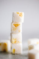A stack of four sugar cubes, some with peach inclusions, on a blurred background.