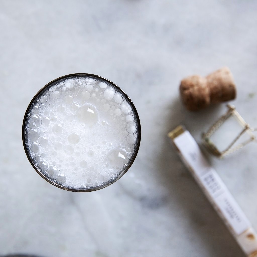 A close-up view of a glass filled with a bubbly beverage, surrounded by a cork and an hourglass on a marble surface.